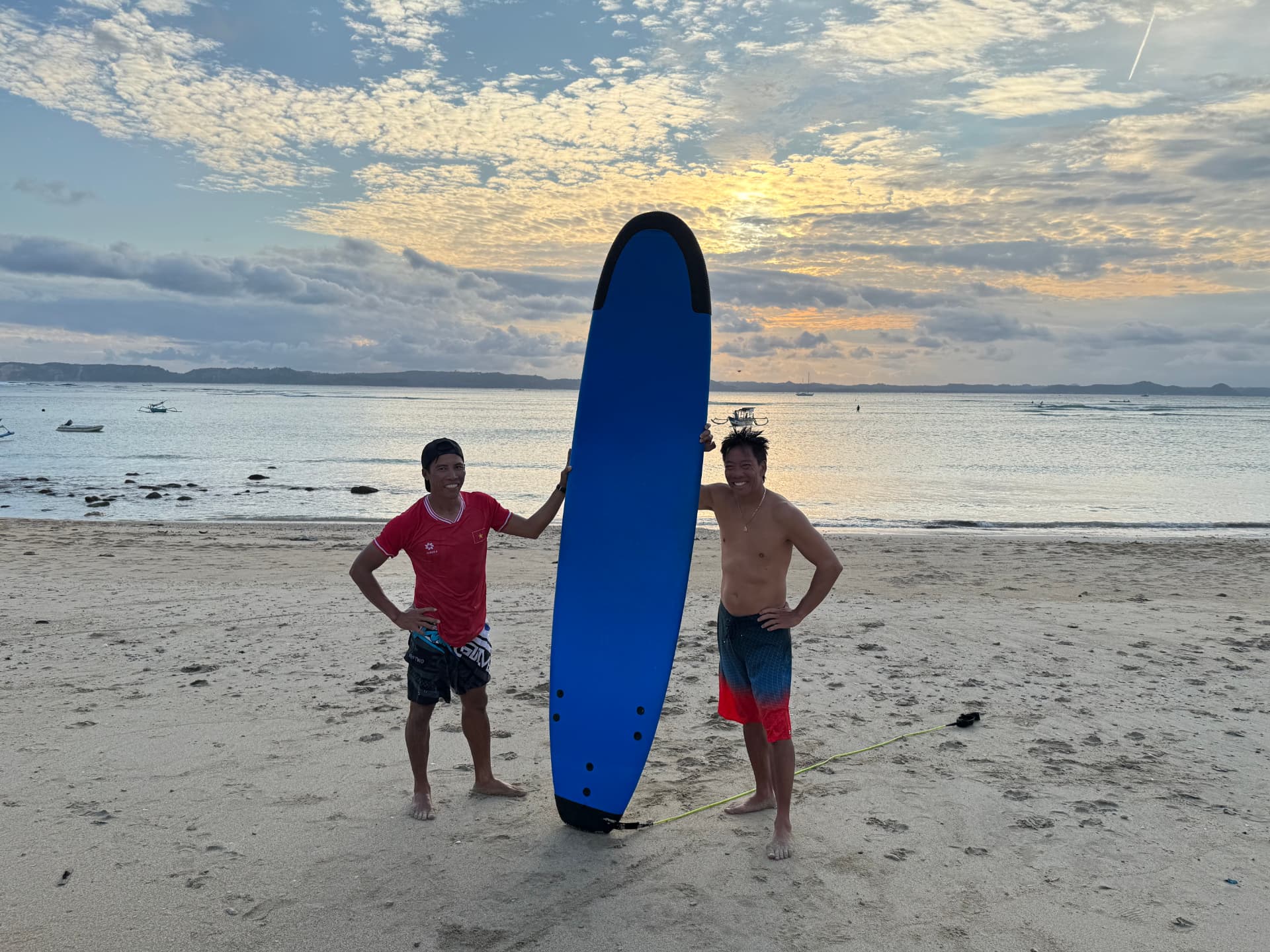 Lý with a surfboard at sunrise on a quiet beach