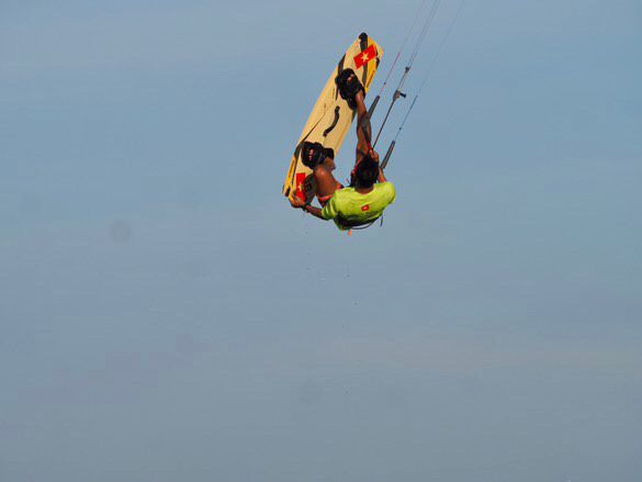 Kitesurfer inverted mid-backroll above the sea