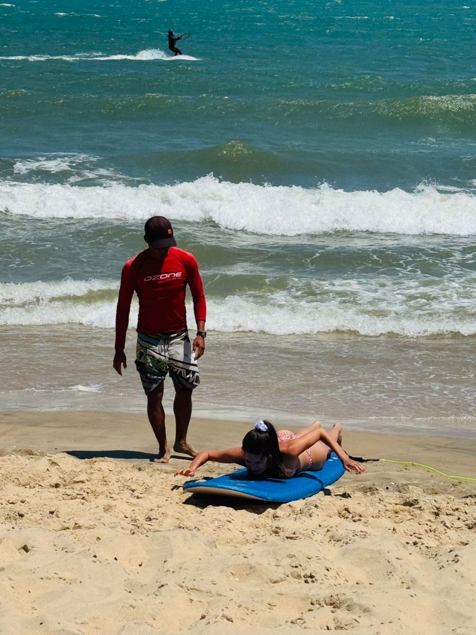 Surf instructor watching a student practice on a board at the water's edge