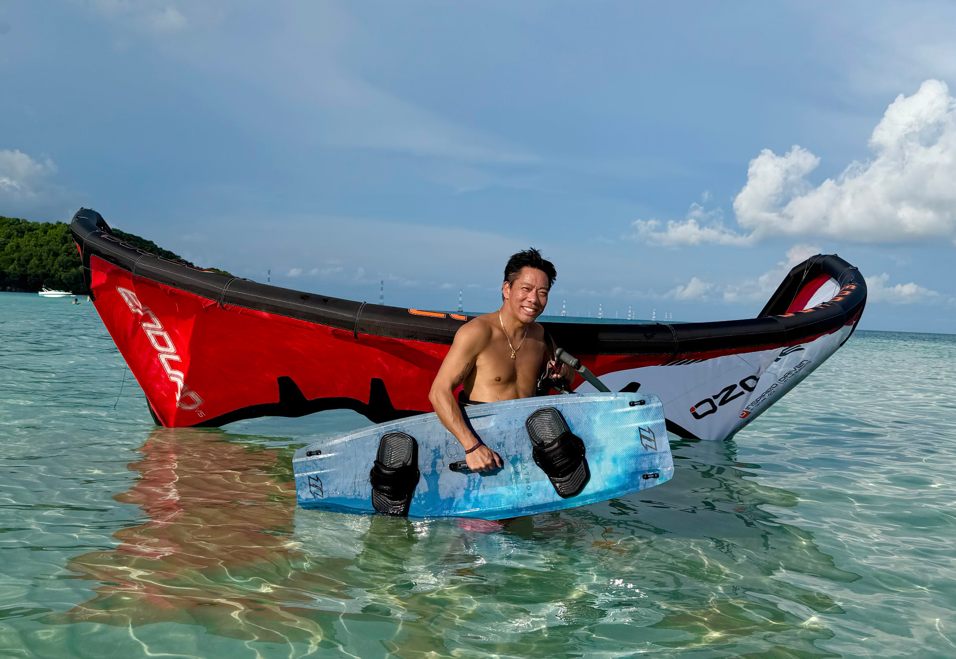 Lý standing in clear turquoise water holding his kiteboard next to an inflated kite