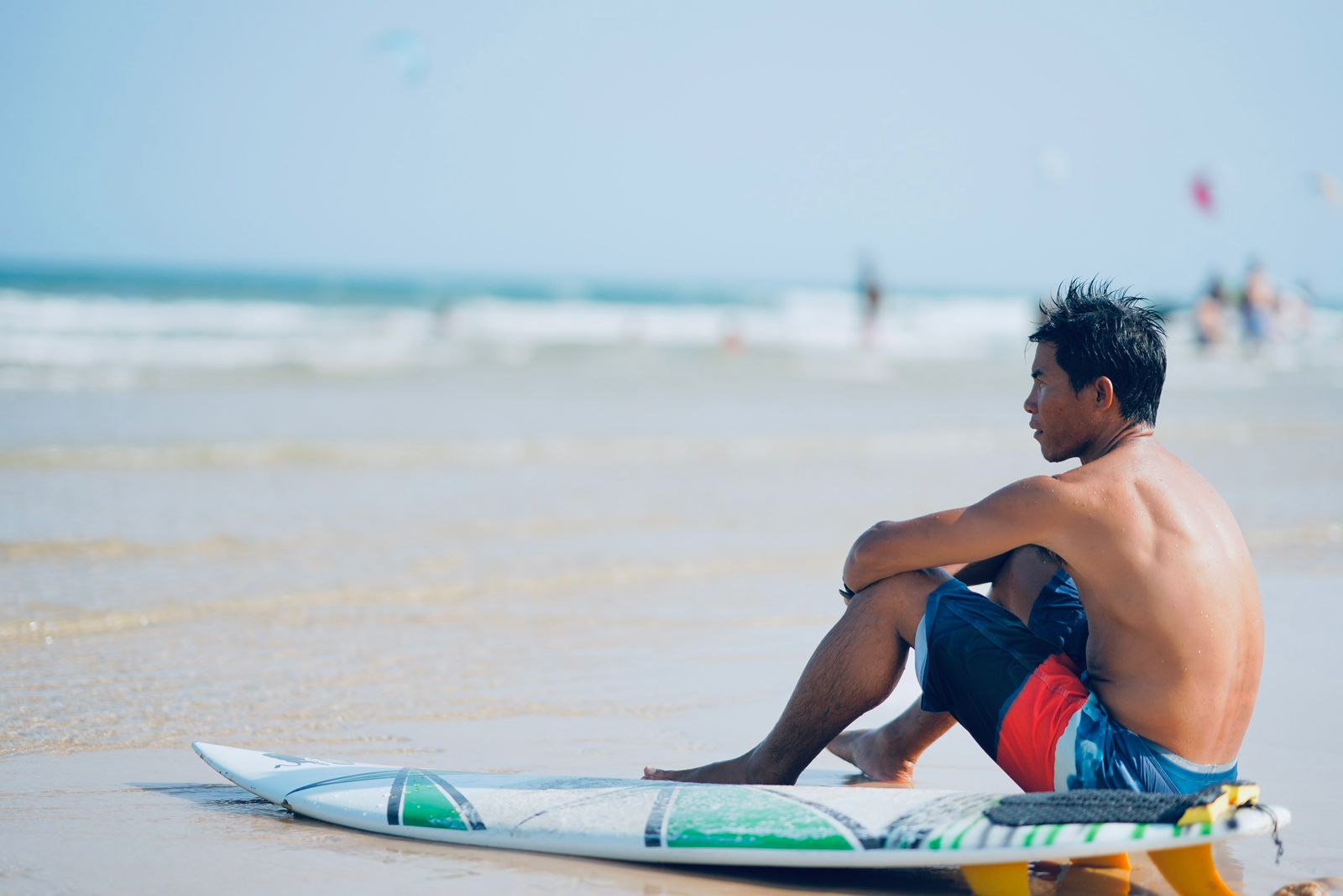Ly sitting on the sand next to his surfboard on Ham Tien beach