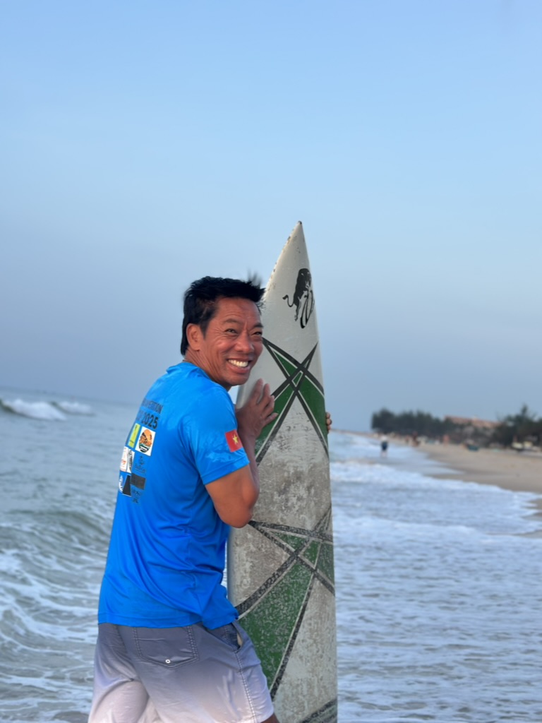 Lý smiling with his surfboard on Ham Tien beach